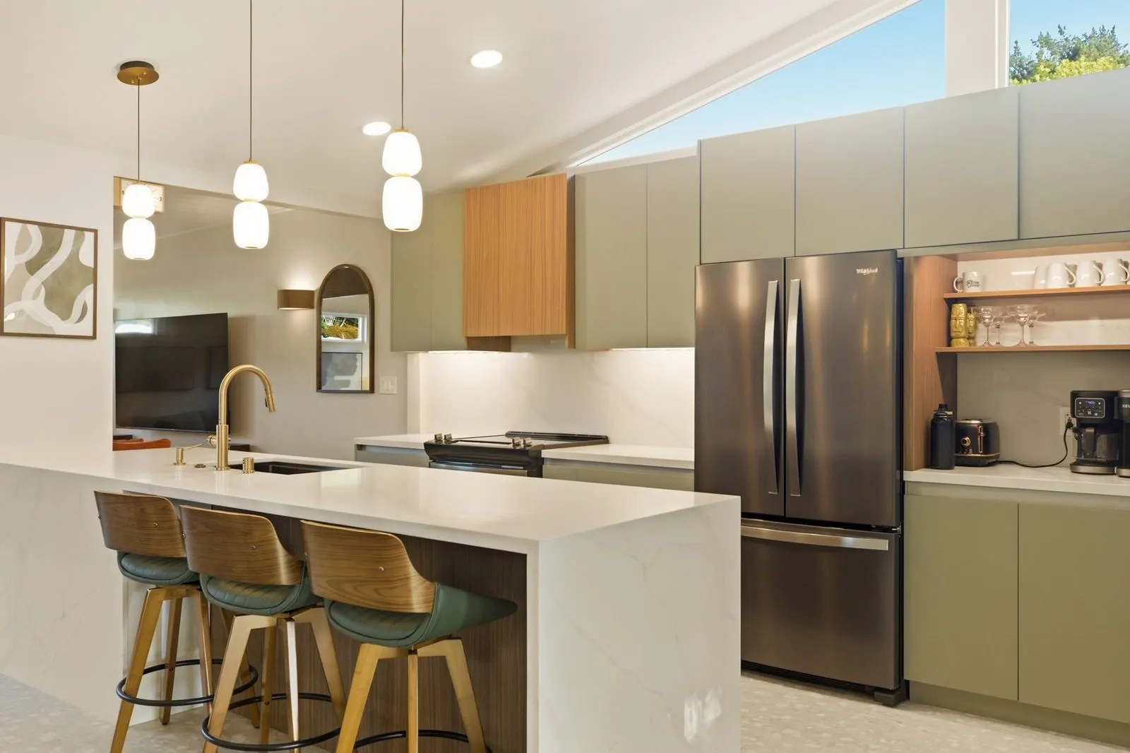 Kitchen with a quartz waterfall island, brass pendants and sage cabinets